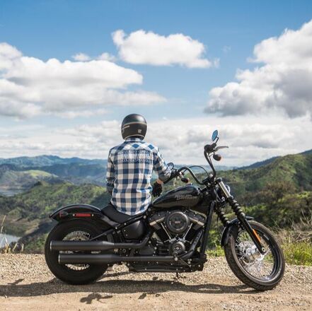Picture of a man in a helmet and blue checkered shirt sitting on a black Harley Davidson motorcycle overlooking a valley