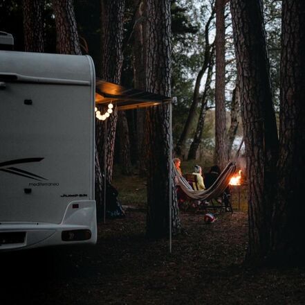 Picture of a Motorhome at a campsite in the mountains with people sitting around a campfire at sunset